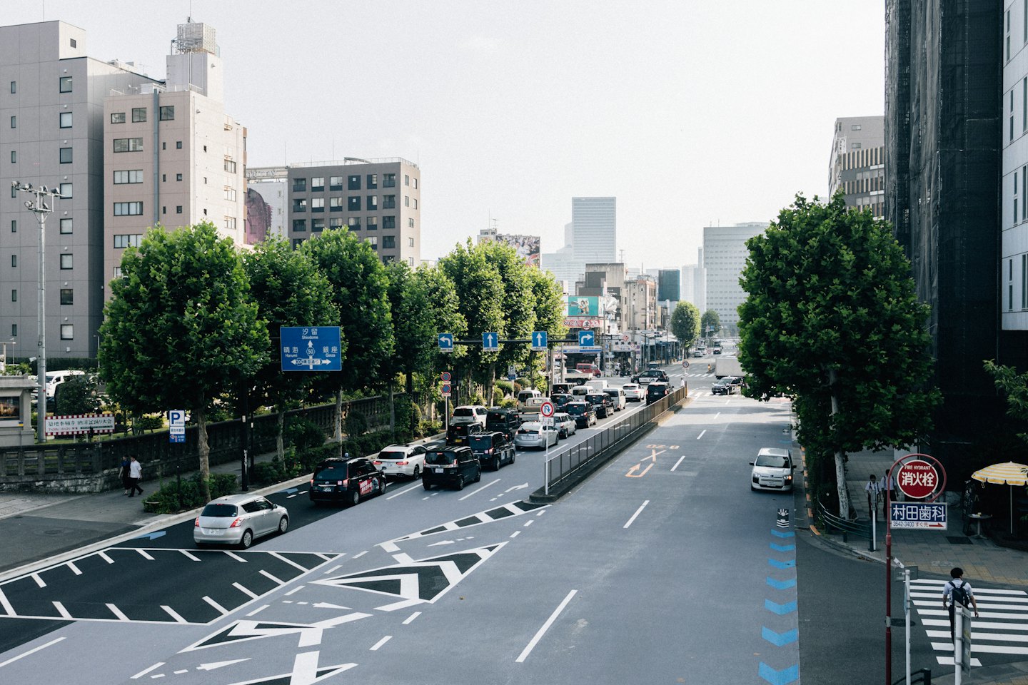 Pedestrians walk along a busy city street lined with buildings.
