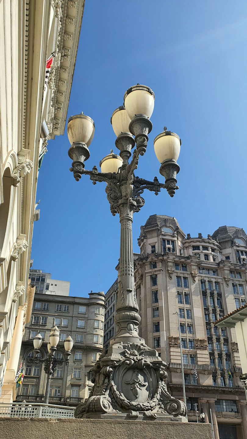 Intricate five-lamp historical lamppost in front of classical buildings.