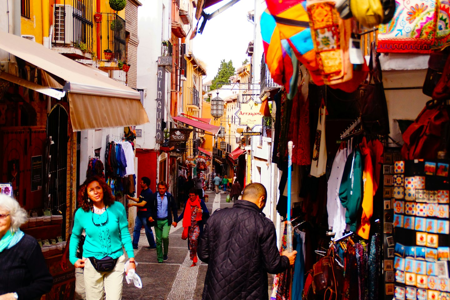 People walk and browse shops along a busy narrow street.